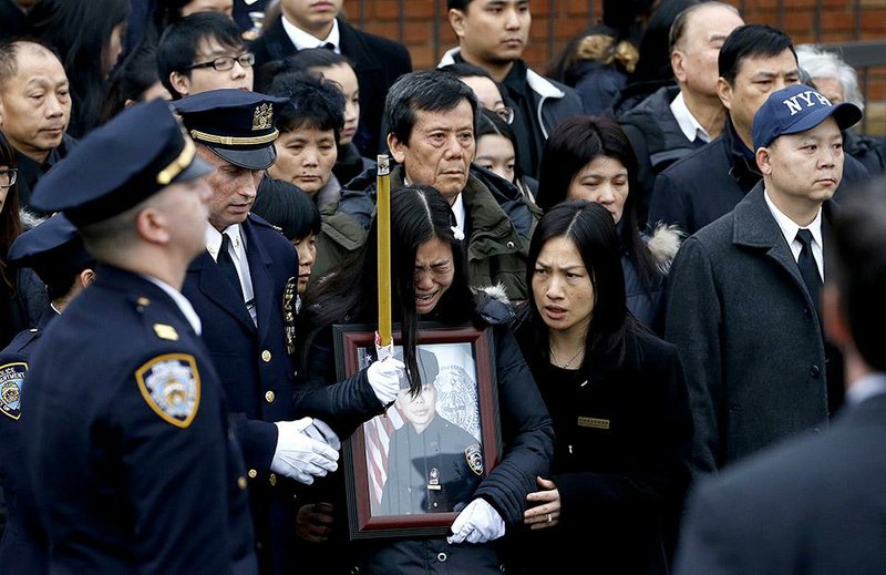 Pei Xia Chen, center, widow of New York City police officer Wenjian Liu, holds a photograph of her husband following funeral services for him at Aievoli Funeral Home, Sunday, Jan. 4, 2015, in the Brooklyn borough of New York. Liu and his partner, officer Rafael Ramos, were killed Dec. 20 as they sat in their patrol car on a Brooklyn street. The shooter, Ismaaiyl Brinsley, later killed himself. (AP Photo/Julio Cortez)