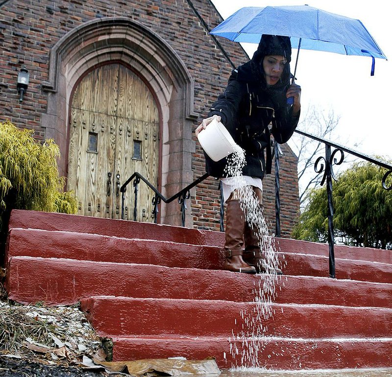 Shanell Taylor pours de-icer on icy stairs and walkways at Chambers United Methodist Church in Trenton, N.J., Sunday, Jan. 18, 2015. Rain "flash-freezing" on roads and sidewalks left an icy glaze under feet and tires across much of the northeast on Sunday, causing crashes that claimed at least four lives. (AP Photo/Mel Evans)