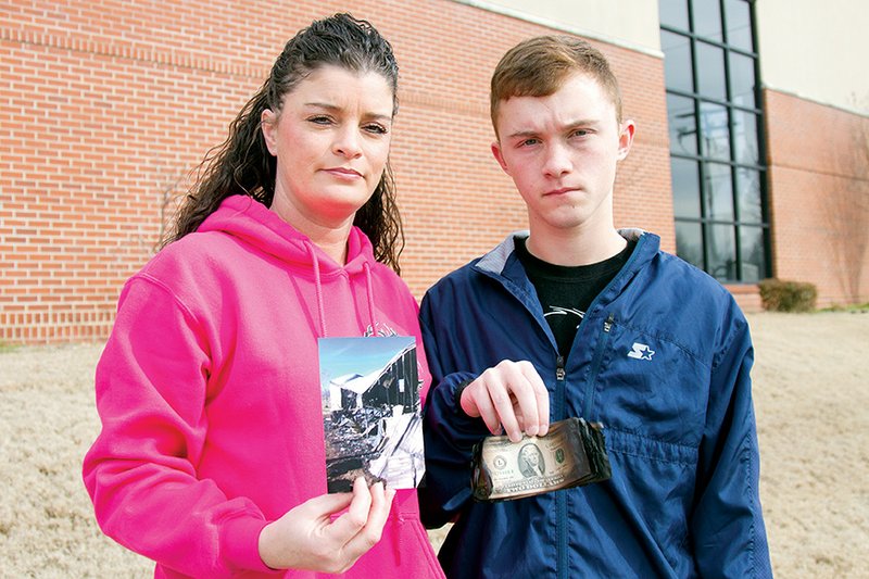 Tara Wilson, left, and Tyler Wilson stand together with reminders of the fire that took their home a couple of weeks ago. Tara holds a photo of the burned home, and Tyler holds charred $2 bills that were part of his money collection that was recovered after the fire.