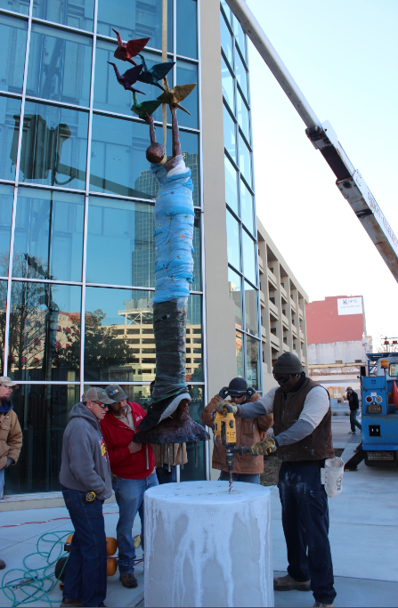 "Peace," a bronze sculpture made by Lori Acott, is lowered into place at 2nd and Main Streets Monday in Little Rock.