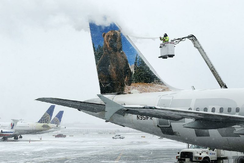 A crewmember de-ices a Frontier Airlines plane at LaGuardia Airport in New York, Monday, Jan. 26, 2015. More than 5,000 flights in and out of East Coast airports have been canceled as a major snowstorm packing up to three feet of snow barrels down on the region. (AP Photo/Seth Wenig)