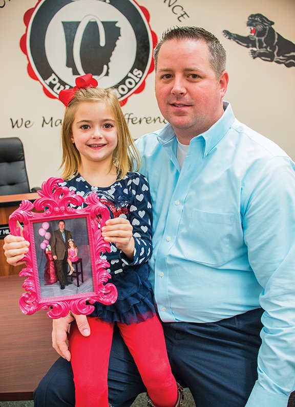 Zoe and her father, Adam Simon, sit with a photo of them from last year’s My Daughter’s Heart Father/Daughter Dance. They plan to attend the dance again this year in Cabot.
