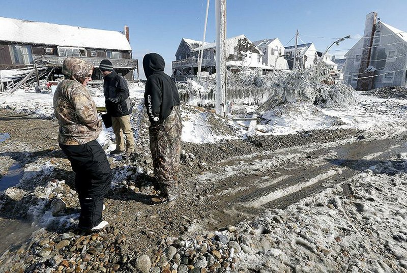Snow, sand, rocks and debris cover the road Wednesday in front of damaged houses in Marshfield, Mass., after this week’s winter storm. 