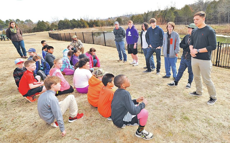 NWA Democrat-Gazette/ANDY SHUPE Gavin McGarrah, 17, (right) a senior environmental and spatial technology student at Fayetteville High School, speaks Friday alongside biology students at Happy Hollow Elementary School and other EAST students during a presentation at the teaching pond behind the school. The pond will be improved with a walking path, aerators, a learning platform and signs using plans developed by EAST students through a grant from Wal-Mart facilitated by the Fayetteville Public Education Foundation.