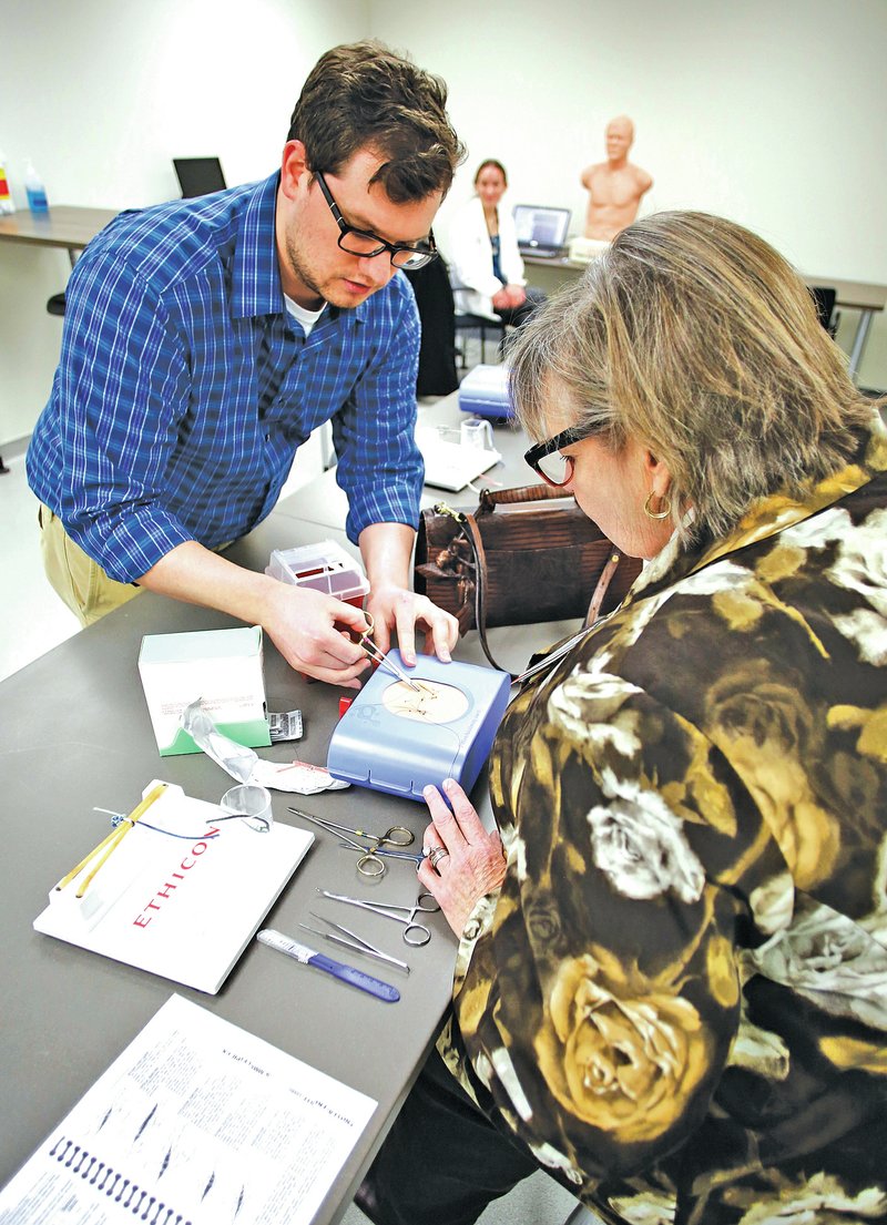 NWA Democrat-Gazette/DAVID GOTTSCHALK Clark Trapp, a fourth-year medical student at University of Arkansas for Medical Sciences Northwest, demonstrates a suture Thursday to Donna Norvell Smith, director of development with the College of Health Professions, at the Pat and Willard Walker Student Clinical Education Center on the Fayetteville campus.