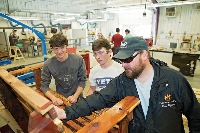Mayflower High School students, from left, Dakota Brown, a senior, and Devon Dycus, a sophomore, help agriculture teacher Ron Bigham sand a cedar porch swing to prepare it for staining. The swing was going to be auctioned last week at an FFA fundraiser. The Mayflower School District started its agriculture program in the 2013-14 school year.