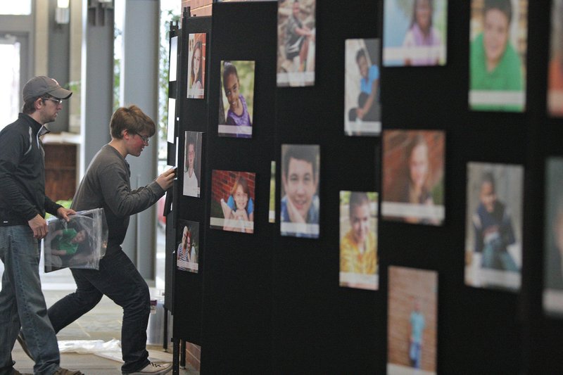 Chris Reaves, left, and Avery Langston hang pictures of children that are available for adoption on the Arkansas Heart Gallery Wall in the El Dorado Conference Center. The event runs through Thursday and is working in conjunction with the Agape House to help bring awareness to the 150 children in the state as well as the 40 in Union County that are available for adoption. The two, along with Karen Langston, coordinator of the CALL in Arkansas, were busy on Monday.