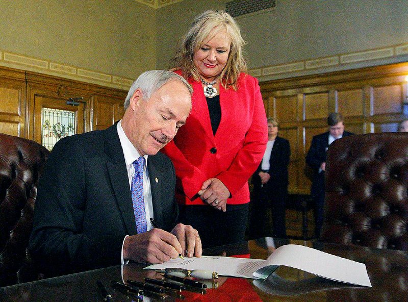 Gov. Asa Hutchinson signs “Andi’s Law” on Wednesday while state Rep. Rebecca Petty, R-Rogers, looks on. The law is named for Petty’s daughter, who was murdered 16 years ago; it allows a murder victim’s family to witness the execution of their loved one’s killer. 