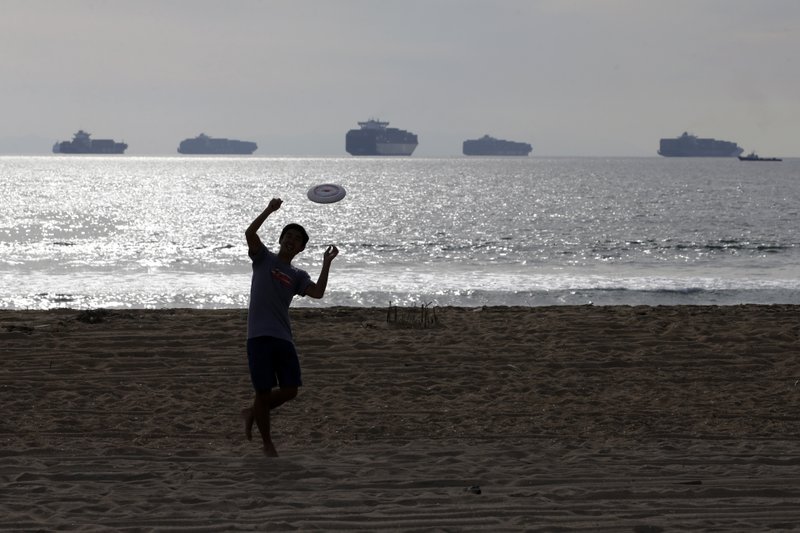 Micah Young catches a frisbee on the beach Friday, Feb. 20, 2015, in Sunset Beach, Calif., as loaded cargo ships are anchored outside the Ports of Long Beach and Los Angeles. Billions of dollars of cargo are sitting on dozens of massive ships anchored outside West Coast ports. They cannot dock because of historically bad cargo bottlenecks at 29 ports that handle about $1 trillion of trade annually, much of it with Asia. 