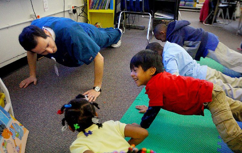Jaylan Osorio (right), a kindergarten student at Romine Elementary in Little Rock, does pushups with classmates Thursday during a lesson on healthy habits taught by University of Arkansas at Little Rock nursing student Charles Wilbanks. 