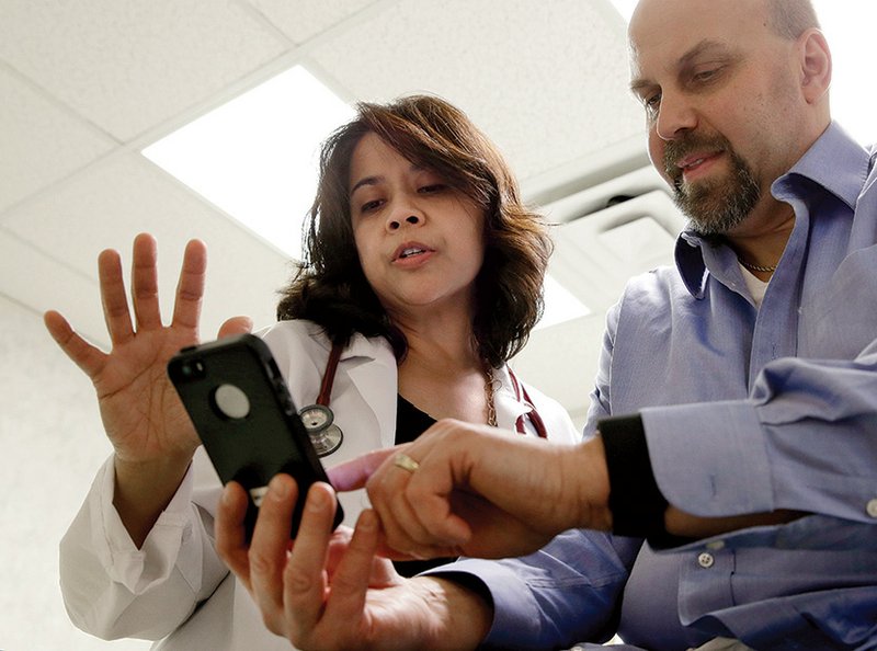 Cardiologist Dr. Sarah Timmapuri (left) looks at data on a smartphone synchronized to a Fitbit Surge worn by patient Gary Wilhelm, 51, during an examination in Hackensack, N.J. Wilhelm joined Hackensack’s app test after he suffered a heart attack in October. 