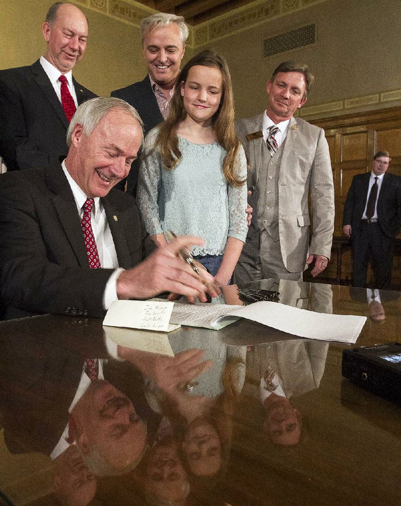 Gov. Asa Hutchinson signs a bill Tuesday requiring Arkansas high schools to offer computer science classes. The governor’s granddaughter, Ella Beth Wengel, joins him for the ceremony.