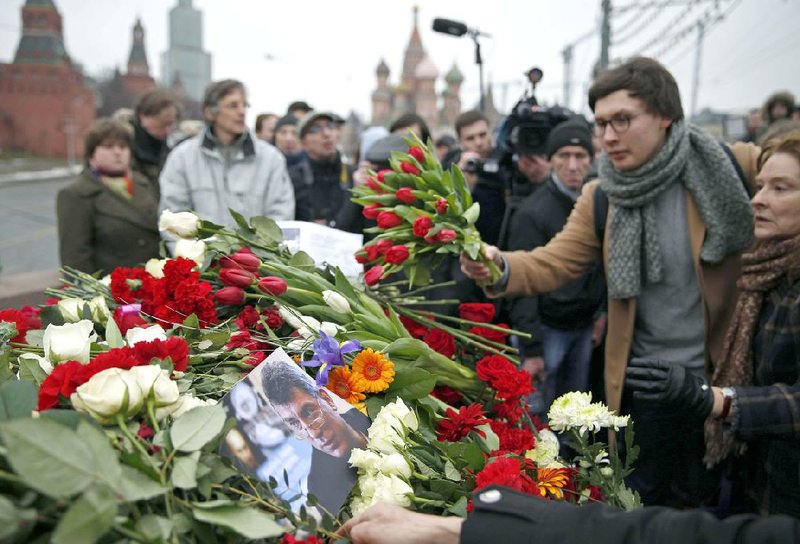People lay flowers at the place where Boris Nemtsov, seen in photo at centre, a charismatic Russian opposition leader and sharp critic of President Vladimir Putin, was gunned down, at Red Square, with St. Basil Cathedral in the back and the Kremlin at left, in Moscow, Russia, Saturday, Feb. 28, 2015. Nemtsov was gunned down Saturday near the Kremlin, just a day before a planned protest against the government. (AP Photo/Pavel Golovkin)