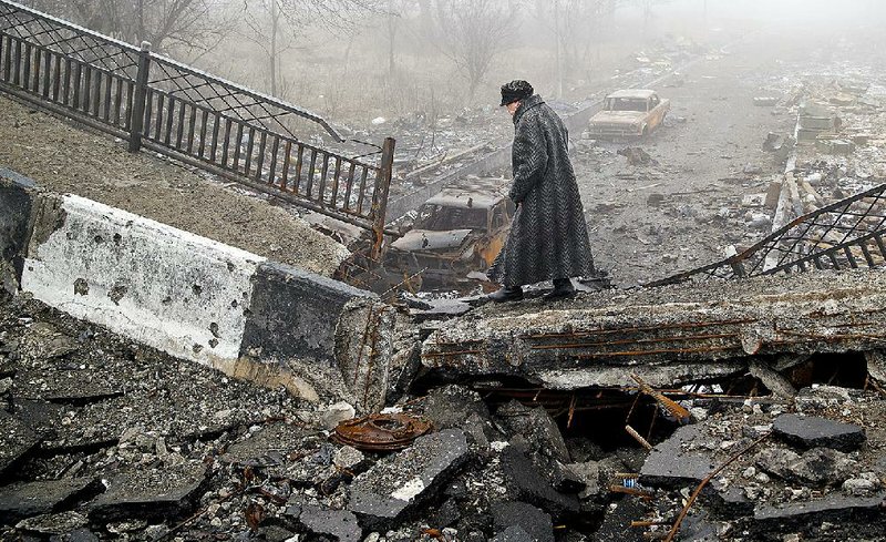 An elderly woman walks across a destroyed bridge, fallen onto the road towards the airport, the scene of heavy fighting in Donetsk, Ukraine, Saturday, March 1, 2015.  The recent pullback of some weapons from the line separating government and rebel forces in Ukraine seems to have boosted the prospects for peace, although both sides are warning of their readiness to resume fighting if necessary. (AP Photo/Vadim Ghirda)