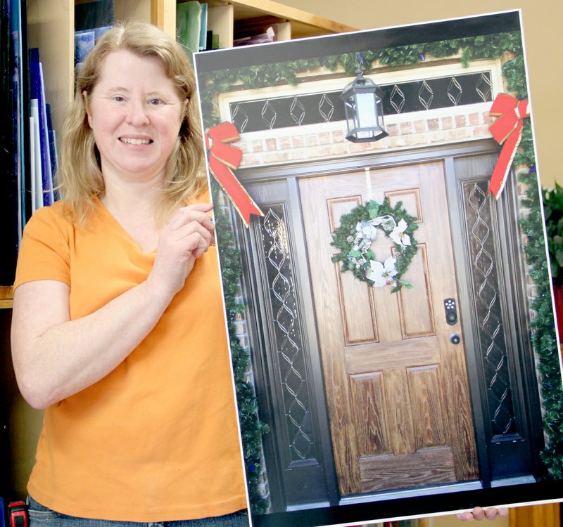 PHOTOS/LYNN KUTTER ENTERPRISE-LEADER Beth Erbe with Cutting Edge Glass & Frame shows a large, matted photo of one of the company&#8217;s projects. The business&#8217; specialty is dressing up front entrances with beautiful leaded-glass artwork. This project has decorative glass above the front door and on both sides.