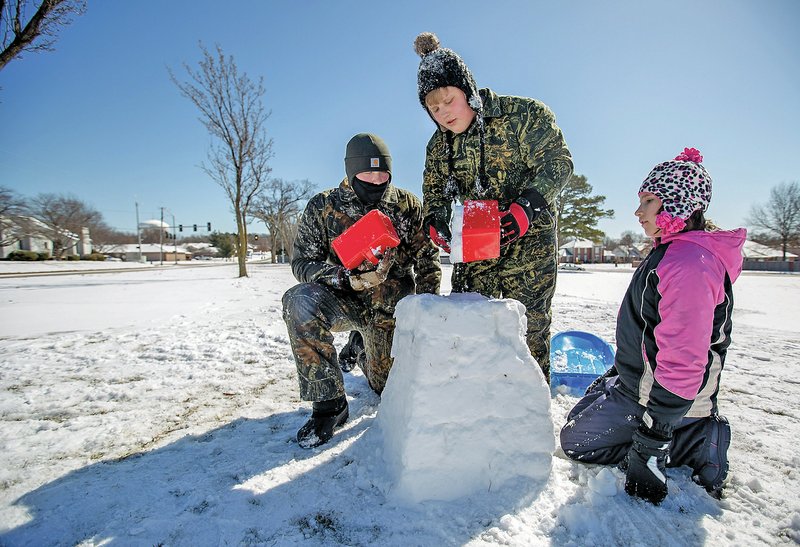 Micah Hulvey (from left), 15, Mitchell Hulvey, 13, and Mikayla Hulvey, 11, build a snow fort Thursday at Elmwood Middle School in Rogers. The siblings were out playing in the snow with their father, Wes Hulvey, all of Rogers.