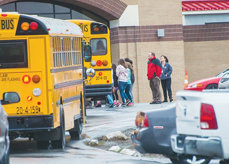 Students bundle up and take cover from the wind and rain as they board a school bus at Cabot High School.