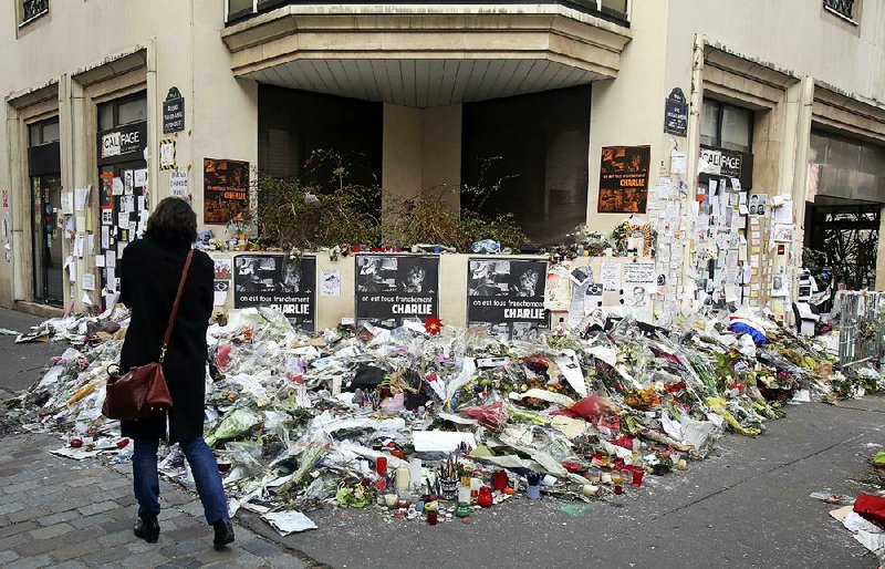 A woman looks at flowers laid near the headquarters of magazine Charlie Hebdo in Paris, Friday Feb. 6, 2015. Brothers Said and Cherif Kouachi killed 12 people in a terror attack at the offices of French satirical publication Charlie Hebdo on Jan. 7. The two gunmen, were killed by French police two days later. (AP Photo/Remy de la Mauviniere)