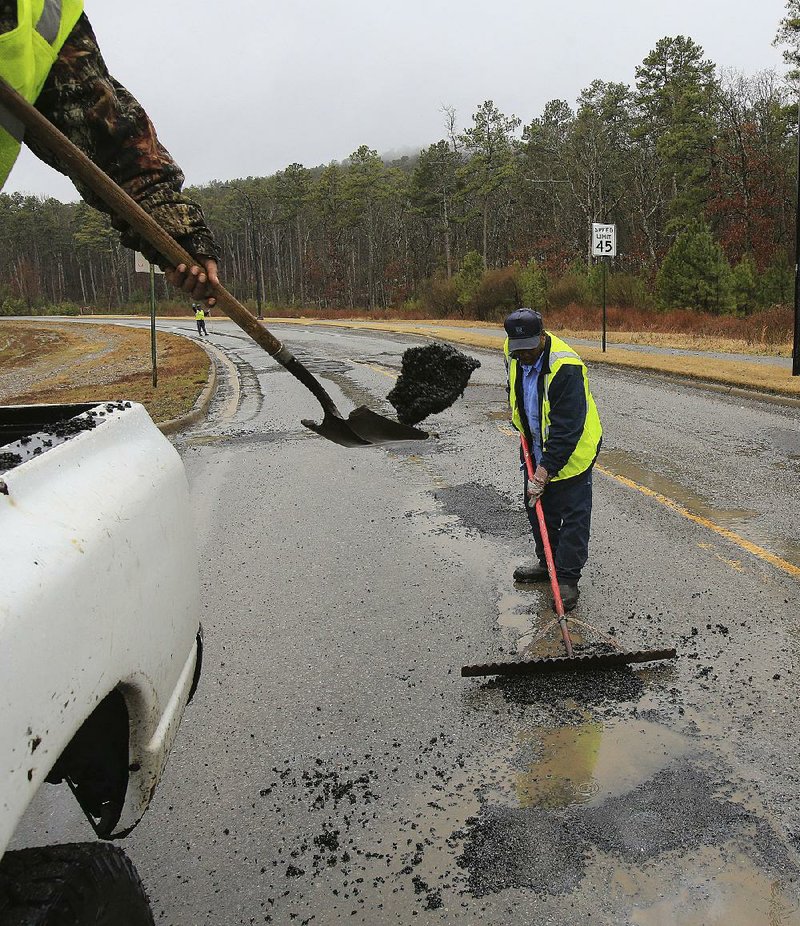 Arkansas Democrat-Gazette/STATON BREIDENTHAL --3/9/15-- Ricky Love (left) of the Little Rock Public Works Department throws a shovel full of asphalt into a pothole Monday on Rahling Road as James Rideout Sr. rakes the material into the hole. 