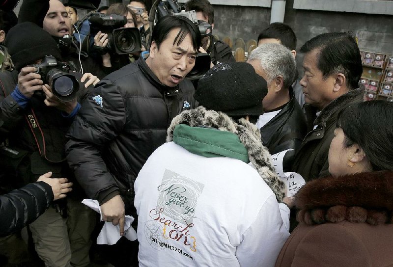 A policeman grabs papers from the relatives of passengers on board the Malaysia Airlines Flight 370 that went missing on March 8, 2014, after they showed the papers to journalists near Yonghegong Lama Temple in Beijing Sunday, March 8, 2015. Families of the 239 people on board the flight 370 on Sunday were marking the anniversary of the plane's disappearance with a vow to never give up on the desperate search for wreckage and answers to the world's biggest aviation mystery. (AP Photo/Andy Wong)