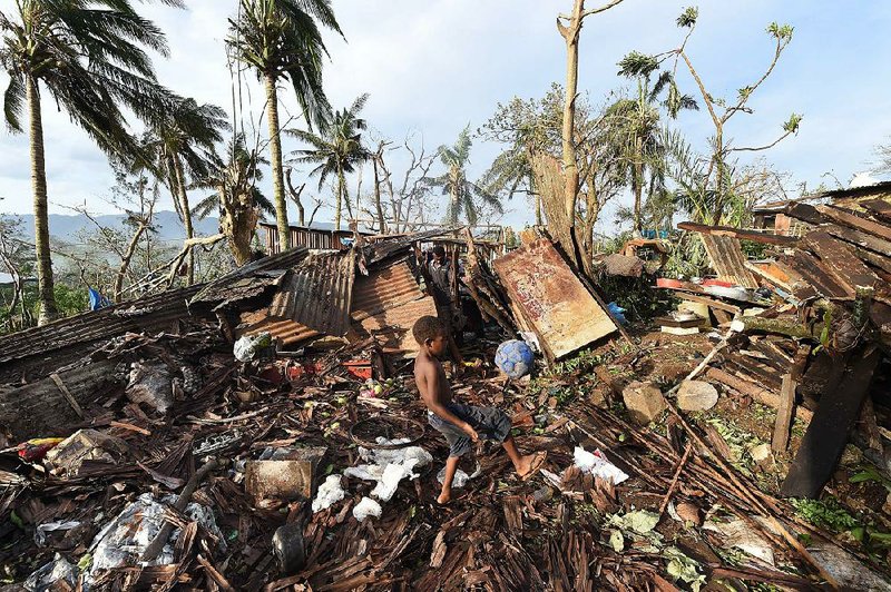 A boy named Samuel kicks a ball through the ruins of his home as his father, Phillip (at back), picks through the debris Monday in Port Vila, Vanuatu, in the aftermath of Cyclone Pam. 