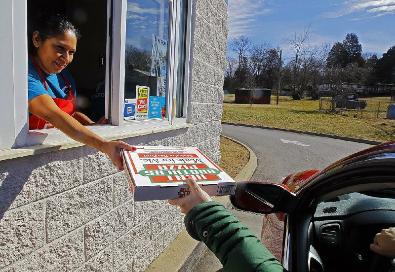 In this Feb. 6, 2015 photo, Maria Witkowski hands a Hunt Brothers Pizza from the drive-thru window to a customer at the Rightway Foodmart in Andersonville, Tenn. Hunt Brothers Pizza is quietly winning over the rural South by slipping into places big-name pizza chains probably couldn’t survive. (AP Photo/Wade Payne)
