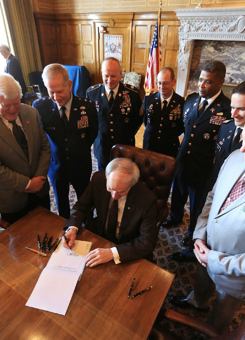 Gov. Asa Hutchinson on Tuesday signs Senate Bill 731, which changes the rules on who is allowed to receive assistance from the state’s Military Family Relief Trust Fund. Behind him are (from left) state Sen Bobby Pierce, D-Sheridan; Maj. Gen. Mark Berry, adjutant general of the Arkansas National Guard; Com mand Sgt. Maj. Steven Veazey; Chief Warrant Officer Donald Kinder; and Maj. Anthony Sanders.