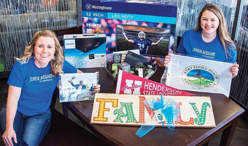 Jessie Willett, left, and Leah Sexton are co-chairmen of the Junior Auxiliary of Arkadelphia’s planning committee for the JA’s April 11 charity ball, A Night With Gatsby. They are shown here with a variety of items that will be available in a silent auction at the event. Patrons will have a chance to buy raffle tickets for the pictured flat screen TV and Blu-Ray DVD player.