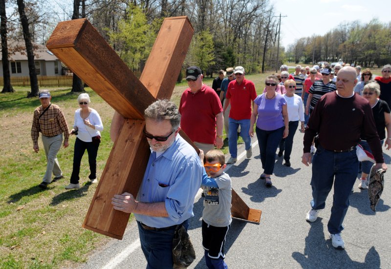 NWA Democrat-Gazette SAMANTHA BAKER Worshipers walk behind Dale Richardson (from left) and Cooper Mclean as they carry a large cross down Glasgow Road in Bella Vista Friday, during a Cross Walk in honor of Good Friday last year. The members of Highlands United Methodist church ook turns dragging the homemade cross on wheels approximately half a mile to simulate Jesus&#8217; own walk. Christians will remember this week the events of Holy Week, the days leading up to the Crucifixion.