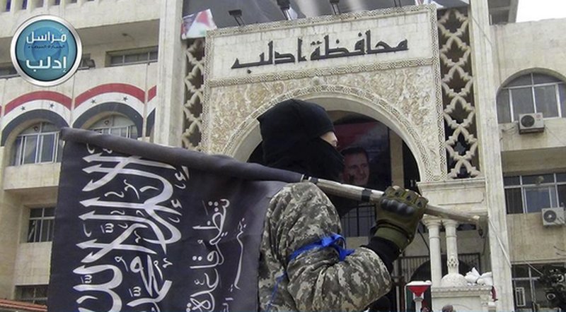 In this image posted on the Twitter page of Syria's al-Qaida-linked Nusra Front on Saturday, March 28, 2015, which is consistent with AP reporting, a fighter from Syria's al-Qaida-linked Nusra Front holds his group flag as he stands in front of the governor building in Idlib province, north Syria. Al-Qaida's affiliate in Syria, the Nusra Front, captured most of the northwestern city of Idlib from government forces Saturday, sweeping into neighborhoods in the center of the city in a powerful blow to President Bashar Assad's government, opposition activists and the group said.