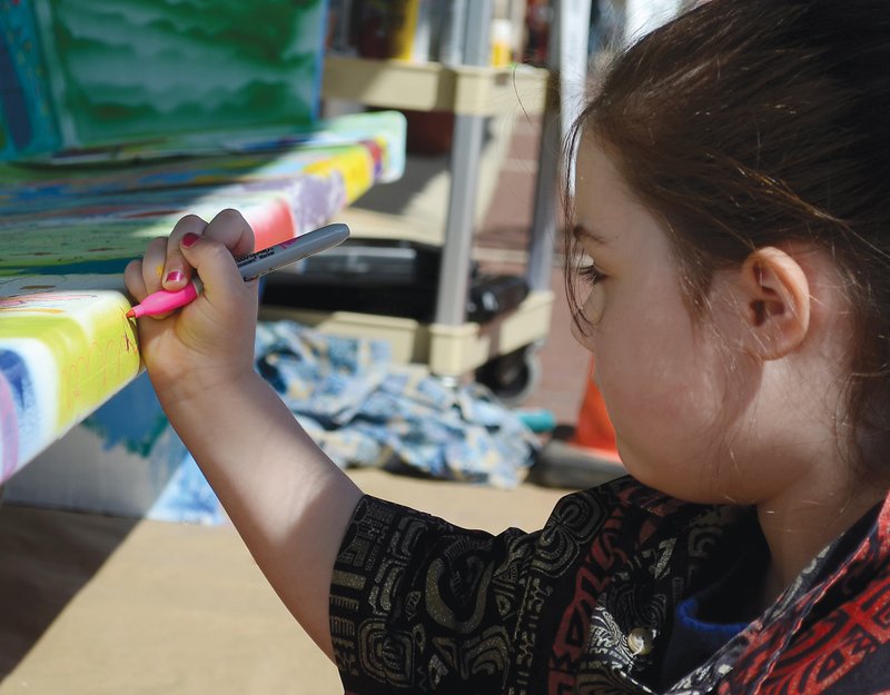 Anna Faith Morgan, 6, draws on the downtown bench in front of Creative Means Studio on Main Street, Friday. Owner Mike Means paints the bench white periodically to allow passersby to add to the unusual canvas.