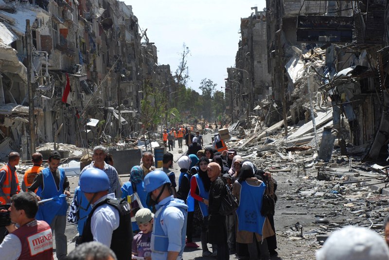 This picture taken on Thursday, April. 24, 2014 and provided by the United Nations Relief and Works Agency for Palestine Refugees in the Near East (UNRWA), U.N relief workers with blue helmets and vests stand next of residents of the besieged Palestinian camp of Yarmouk, right, who stand in line to receive aid food distributed by UNRWA, on the southern edge of the Syrian capital Damascus, Syria. On Wednesday, April. 1, 2015 Islamic State militants infiltrated the Palestinian refugee camp of Yarmouk in the Syrian capital marking the deepest foray yet by the extremist group into Damascus Syrian opposition activists and Palestinian officials said. 