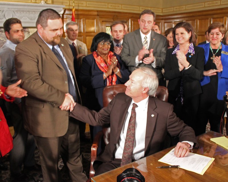 Gov. Asa Hutchinson shakes hands with Rep. Bob Ballinger after he signed Senate Bill 975 into law on Thursday.