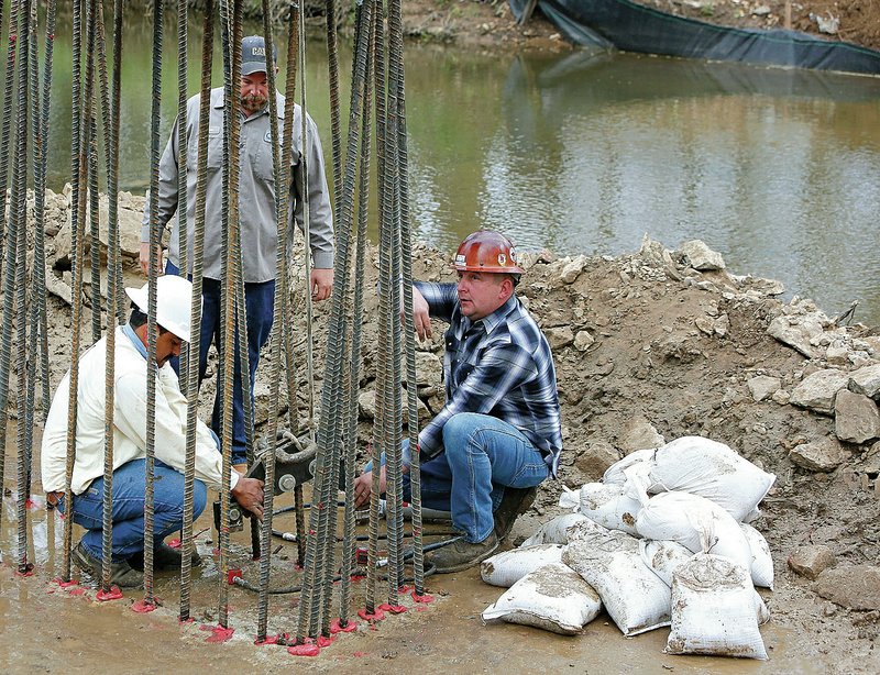 NWA Democrat-Gazette/DAVID GOTTSCHALK Hayden Wagnon (center), with the Washington County Road Department, watches Eusebio Ortez (left), a technician with GTS, and Dale Barnett, structural steel inspector, do a hydraulic pressure test Thursday on rebar attached to the footings of piers for the Stonewall Bridge on Stonewall Road.