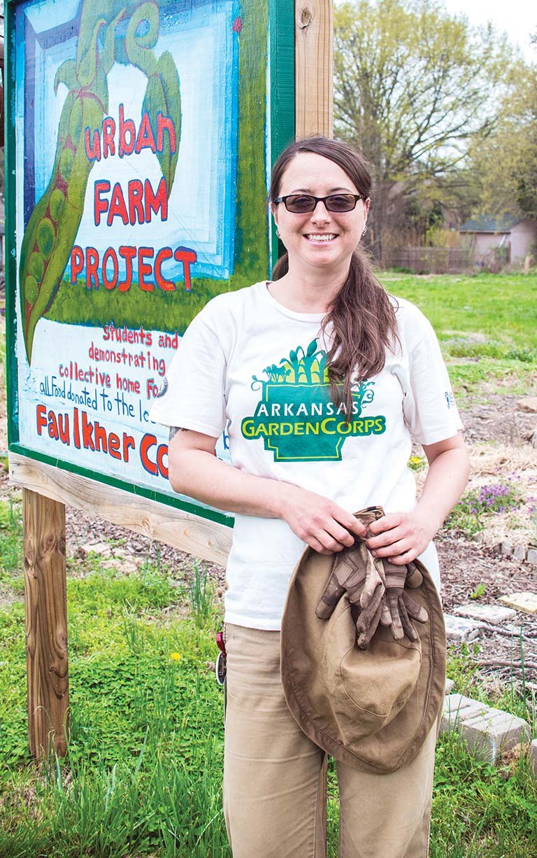 Crystal Bowne of Conway, an Arkansas GardenCorps service member, stands beside a sign for the Faulkner County Urban Farm Project. The community garden is immediately behind the Faulkner County Library, and Bowne staffs the garden several hours a week. The garden, a project of The Locals, a nonprofit organization, provides food for a local food pantry and also serves as a teaching tool for growing food sustainably.