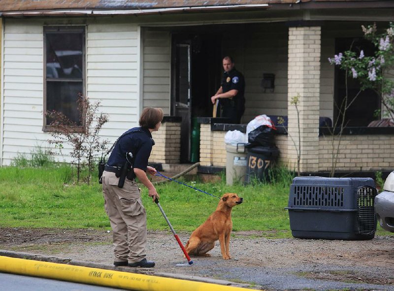 Jessica Beins, with North Little Rock Animal Control, tries to coax a dog to go with her Tuesday morning at the scene of a fatal fire at 1307 W. 16th St. in North Little Rock. The dog was found in a pet carrier inside the house. A woman and man were found dead in the attic. 