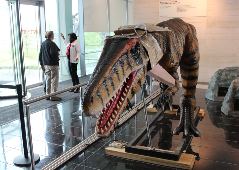 Vanessa Taylor, a volunteer at the Clinton Presidential Center, speaks with visitors to the museum beside a large, animatronic Herrerasaurus being installed as part of a new dinosaur exhibit.