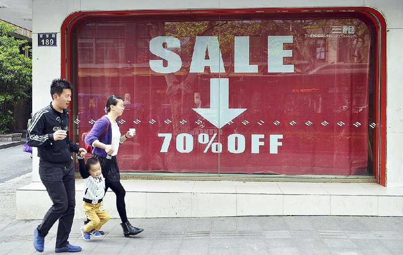 Residents pass a textile shop offering huge discounts in Hangzhou in east China’s Zhejiang province Wednesday. China’s economic slump deepened as manufacturing and retail sales cooled in the first quarter. 