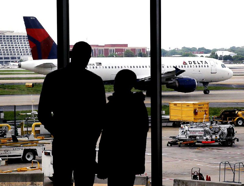 In this Tuesday, April 14, 2015 photo, travelers watch as a plane taxis at Hartsfield-Jackson Atlanta International Airport in Atlanta. After years of steadily-rising airfare, travelers this summer can expect a tiny bit of relief, a really tiny bit. The average roundtrip domestic ticket this summer now stands at $454, down $2.01 from last summer. Vacationers to Europe will fare better with tickets down 3 percent to $1,619, about $50 less. (AP Photo/Charles Rex Arbogast)