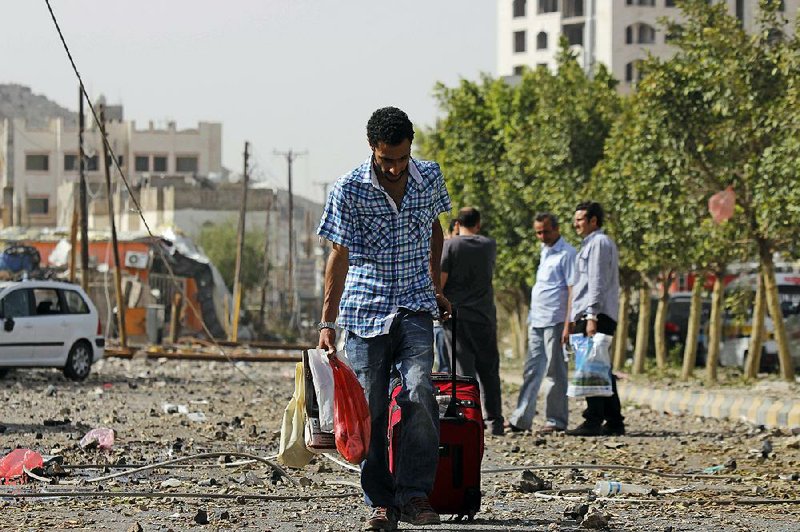 A man carries his belongings on a street littered with debris as he flees from his home after a Saudi-led airstrike against Iran-allied Shiite rebels, known as Houthis, that hit a site of a weapons cache in Yemen's capital, Monday, April 20, 2015. Saudi-led airstrikes on weapons caches in Yemen's rebel-held capital on Monday caused massive explosions that shattered windows, sent residents scrambling for shelter and killed a local TV presenter. (AP Photo/Hani Mohammed)