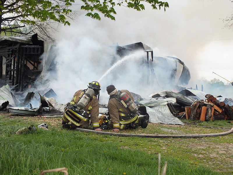 TIMES photograph by Annette Beard Pea Ridge firefighters Jonathan Simpkins, left, and Jordan Hayes, right, spray water on flames at 15991 Patton Road Wednesday morning. The fire destroyed the home and three family pets.