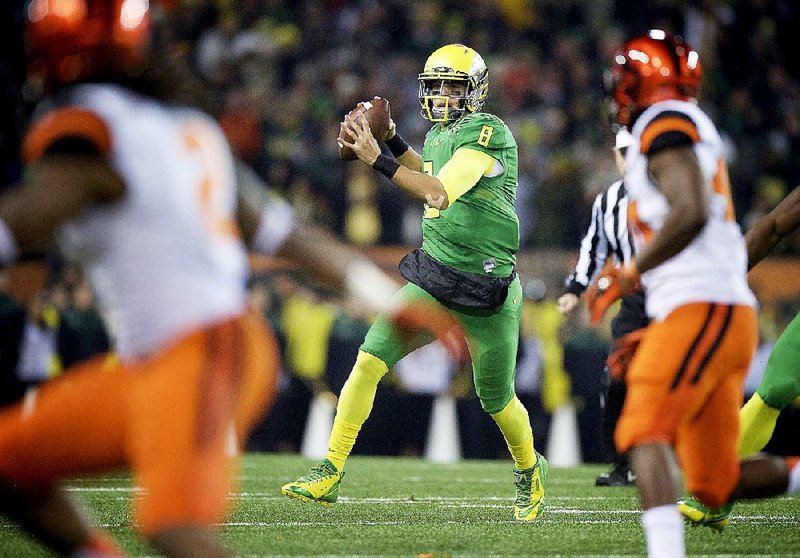 FILE - In this Nov. 29, 2014, file photo, Oregon quarterback Marcus Mariota prepares to throw during an NCAA college football game against Oregon State in Corvallis, Ore. While 26 draft-eligible players have accepted invitations from the NFL to attend the proceedings later this month, Jameis Winston and Mariota are not among them. The two most recent Heisman Trophy winners and highest-profile players in this year's crop have opted to stay home with their families for the April 30-May 2 draft.  (AP Photo/Troy Wayrynen, File)