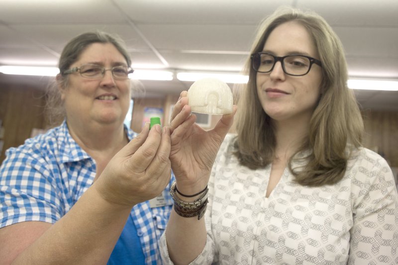 From left,  Venessa Ford, Ward Public Library branch manager, and Meagan Ashcraft, Lonoke/Prairie County Library System project manager, hold up objects made with the system’s 3-D printer.
