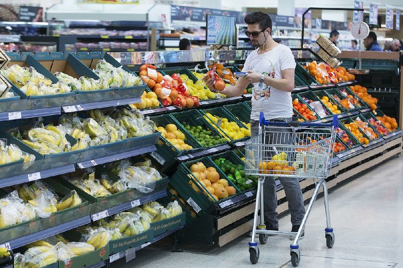 A customer uses a hand-held device to scan a net of oranges as he shops in the fruit and vegetable aisle of a Tesco supermarket, operated by Tesco Plc, in London, U.K., on Monday, April 20, 2015. Tesco's April 22 results will serve as a reminder of the scale of the task still facing new Chief Executive Officer Dave Lewis after his decision to close dozens of stores, cancel some openings, consolidate head offices and cut prices on hundreds of branded goods. Photographer: Jason Alden/Bloomberg