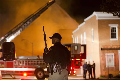 An officer stands near a blaze, Monday, April 27, 2015, after rioters plunged part of Baltimore into chaos, torching a pharmacy, setting police cars ablaze and throwing bricks at officers.