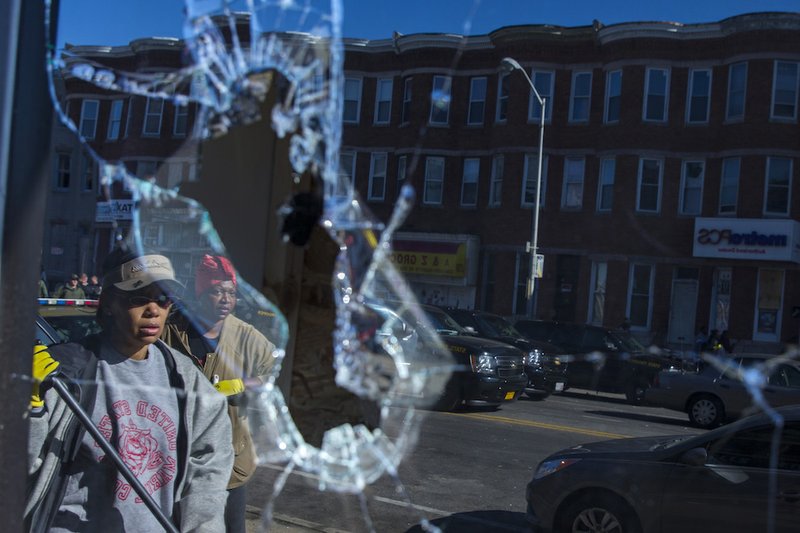 Residents, reflected off broken glass, clean up after an evening of riots following the funeral of Freddie Gray on Tuesday, April 28, 2015, in Baltimore. The violence that started in West Baltimore on Monday afternoon had spread to East Baltimore and neighborhoods close to downtown and near Camden Yards. 
