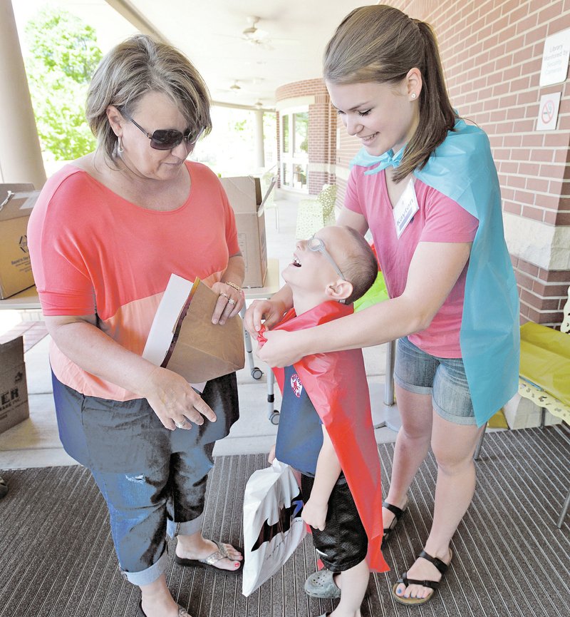NWA Democrat-Gazette/BEN GOFF Kayton Coffee (from right), a library volunteer, fits a cape on Maddux Griesenauer, 6, Saturday as his grandmother Diana Lovell looks on after arriving for the inaugural Bentonville Youth Literature Festival and Free Comic Book Day at the Bentonville Public Library.