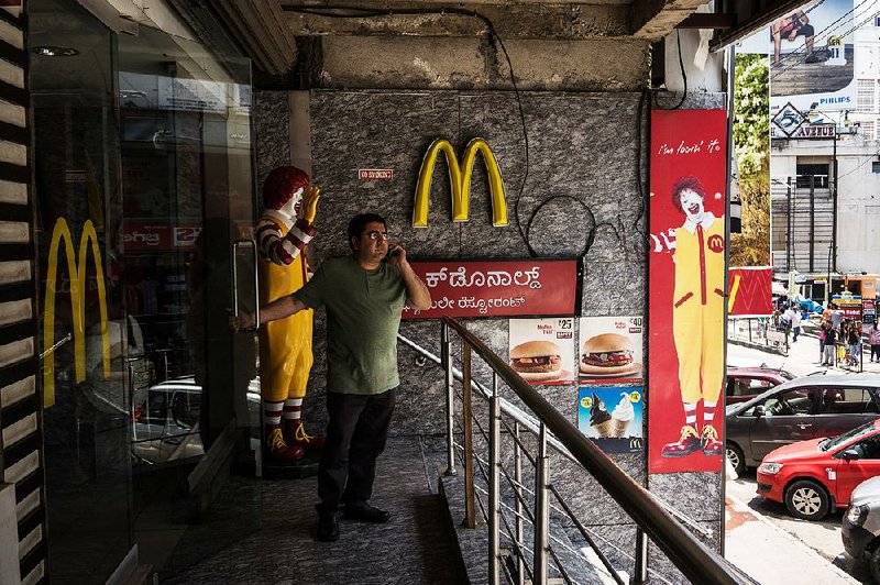 A man speaks on a mobile phone while holding a front door to a McDonald's Corp. restaurant, operated by Hardcastle Restaurants Pvt., on Brigade Road in Bangalore, India on Sunday, May 3, 2015. India's Finance Minister Arun Jaitley is striving for a goods and services levy to subsume a range of federal and state taxes, a step that would make India more of a single market for commerce. Photograph: Sanjit Das/Bloomberg