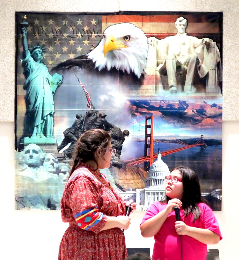 Makayla Hernandez (left) and Amiya Anguiano, two members of the Cherokee Choir, perform hymns and other traditional American songs in the Cherokee language, which is Southern Iroquoian, during Decatur Northside Elementary School&#8217;s &#8220;Traveling Through the U.S.A.&#8221; night April 23. The pair performed in front of a wall poster celebrating America.