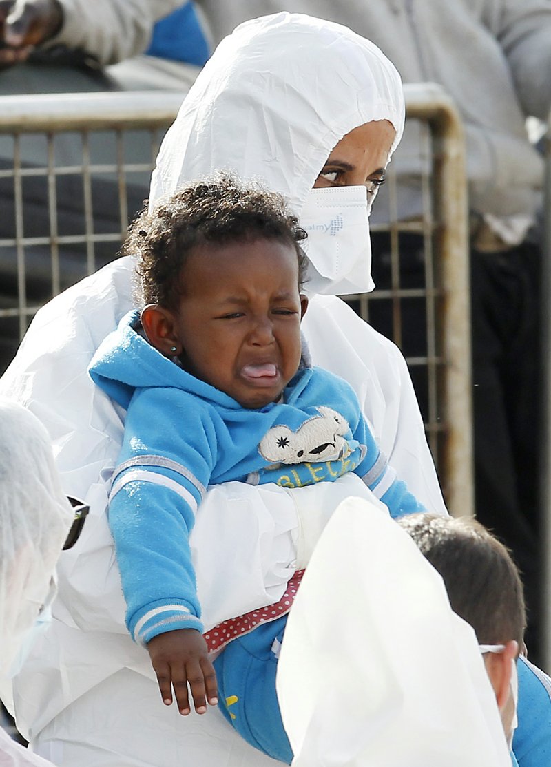 A worker in sanitary outfit holds a crying baby as migrants disembark from the Iceland Coast Guard vessel Tyr, at the Messina harbor, Sicily, southern Italy, Wednesday, May 6, 2015. This weekend saw a dramatic increase in rescues as smugglers in Libya took advantage of calm seas and warm weather to send thousands of would-be refugees out into the Mediterranean in overloaded rubber boats and fishing vessels.
